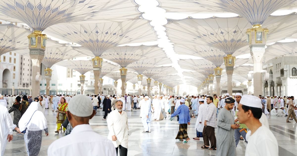 Pilgrims walking beneath the iconic white shading umbrellas in the courtyard of Masjid al-Nabawi in Medina, a destination included with your Umrah visa UK.