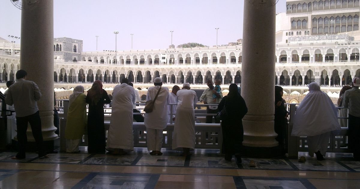 Pilgrims looking out from the colonnades over the Grand Mosque (Masjid al-Haram) courtyard, a serene view included in all cheap Umrah packages UK.